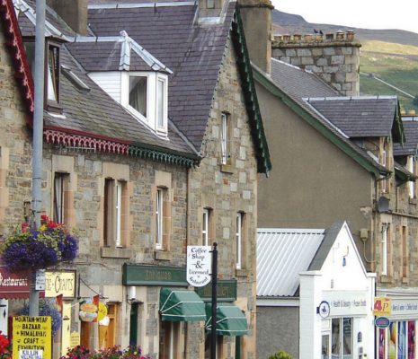 killin-village-main-street-old-stone-victorian-houses-with-colourful-shop-entrances-and-flowers-high-mountains-visible-behind-on-right
